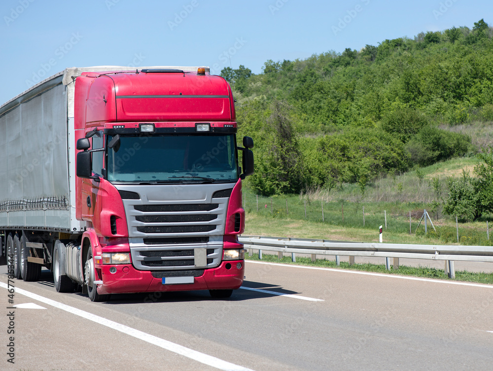 Red Semi-trailer driving along highway. Goods Delivery by roads. Services and Transport logistics