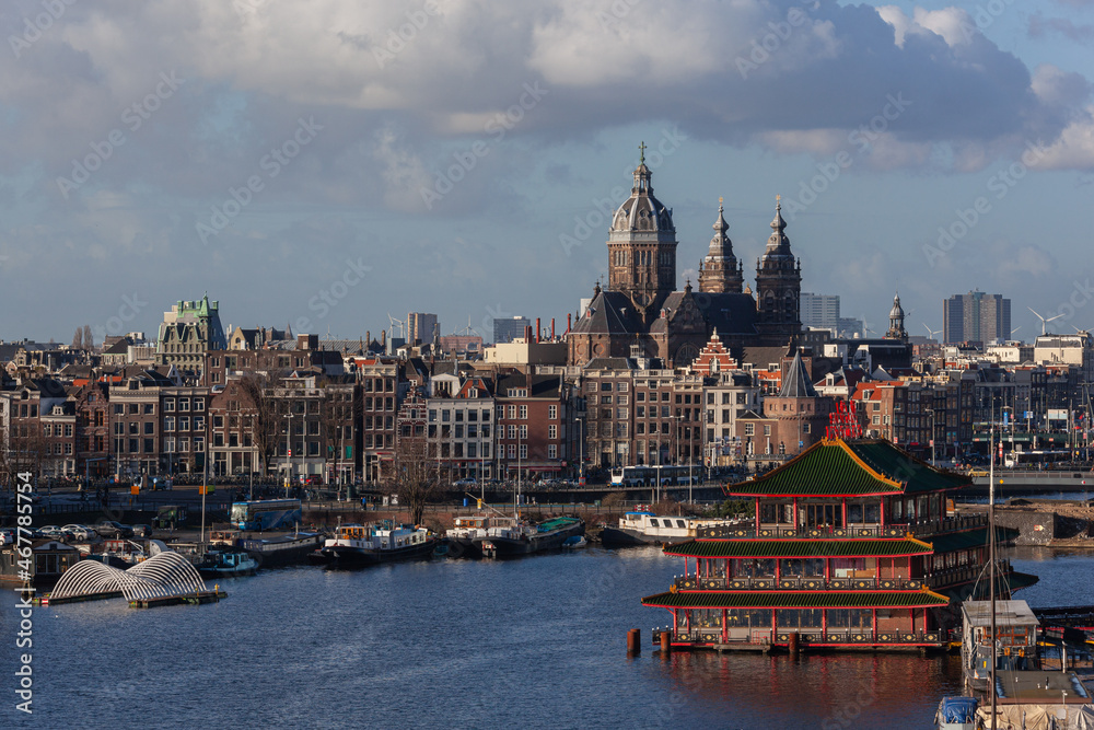 Obraz premium Scenic Amsterdam harbor with boats, ships and famous floating Chinese restaurant against the backgound of historical church and panoramic city view, Netherlands.