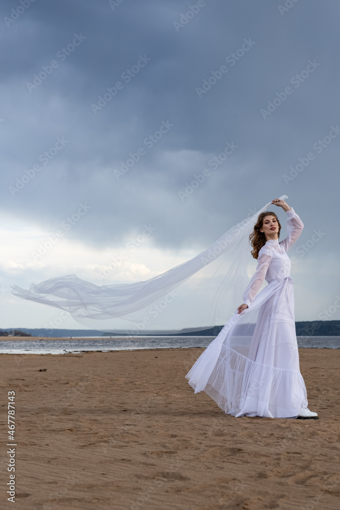 Happy young girl in a white dress on the river bank. Stormy sky in the clouds Happy young girl in a white dress on the river bank. Stormy sky in the clouds
