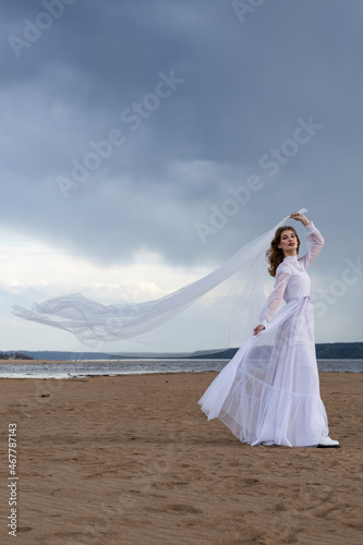 Happy young girl in a white dress on the river bank. Stormy sky in the clouds