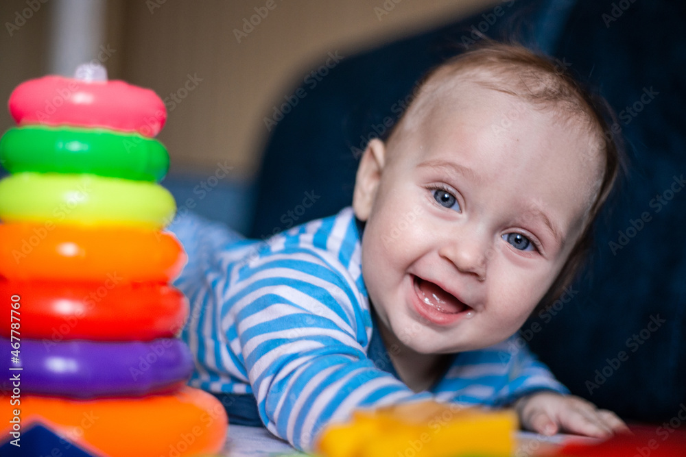 A little kid in a striped suit is lying on his tummy, next to him a children's pyramid and toys. High quality photo A little kid in a striped suit is lying on his tummy, next to him a children's pyramid and toys. High quality photo
