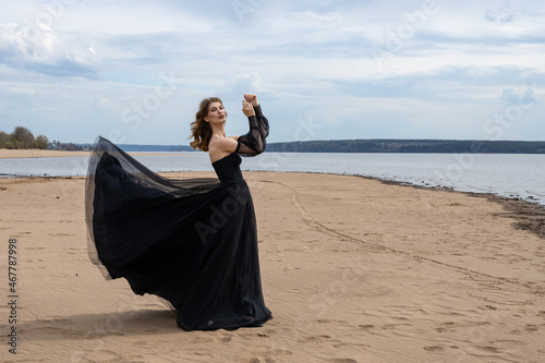 Happy young girl in black dress on the river bank