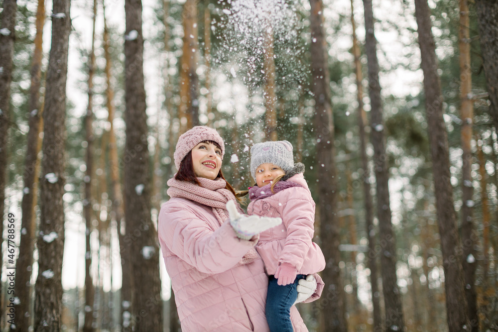 Young mother holding cute little daughter, in a winter forest for a walk. Pretty mom with child on hands, wearing pink coats throwing snow up and laughing. Family in winter forest Young mother holding cute little daughter, in a winter forest for a walk. Pretty mom with child on hands, wearing pink coats throwing snow up and laughing. Family in winter forest