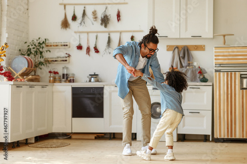 Happy african american family father and little son dancing to music in modern kitchen at home