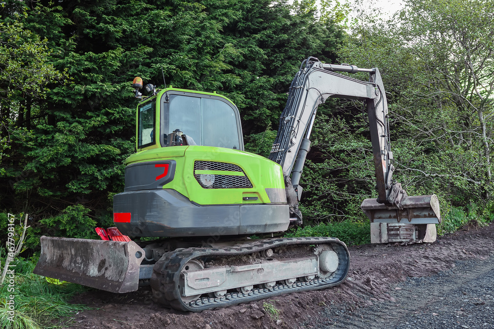 Small bulldozer and excavator by a green forest. Construction site with heavy machinery equipment. Nobody. Road repair concept Small bulldozer and excavator by a green forest. Construction site with heavy machinery equipment. Nobody. Road repair concept