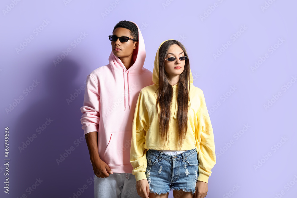 Stylish young couple in hoodies on violet background