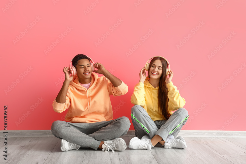 Stylish young couple in hoodies with headphones near pink wall Stylish young couple in hoodies with headphones near pink wall