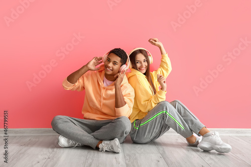Stylish young couple in hoodies with headphones near pink wall