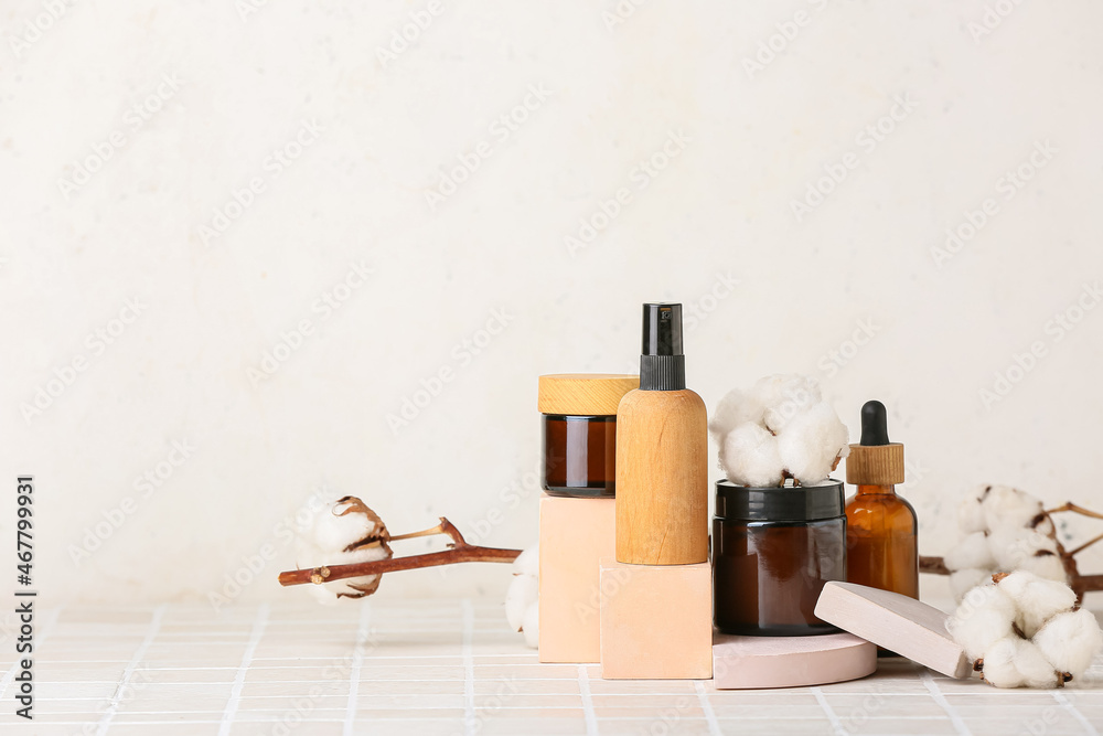 Composition with different cosmetic products and cotton flowers on tile table against light background Composition with different cosmetic products and cotton flowers on tile table against light background