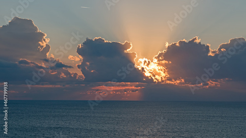 Rays of light shoot from behind clouds in a sunset over the Mediterranean sea