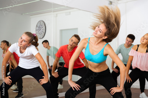 Group of teenage boys and girls exercising with female coach in choreography class..