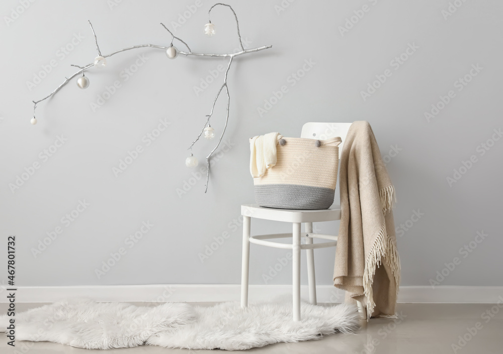 Comfortable chair with plaid, Christmas decor with tree branches and festive balls on light wall in room - obrazy, fototapety, plakaty 