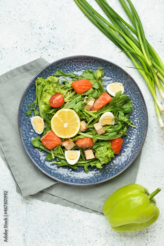 Tasty salad with salmon and vegetables in plate on light background