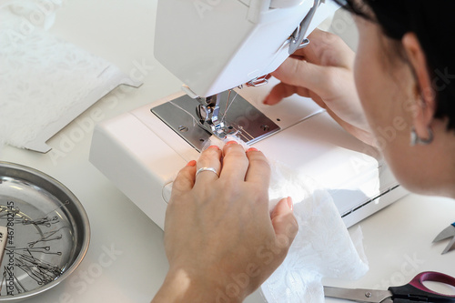 A woman, a European, aged 35-40 years, sews lace white underwear behind a sewing machine. Concept: atelier, sewing hobby, sewing and sewing courses, needlework, handwork.