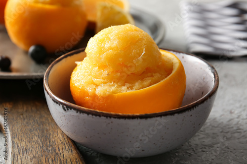 Bowl with tasty ice creams in orange peels on grey background
