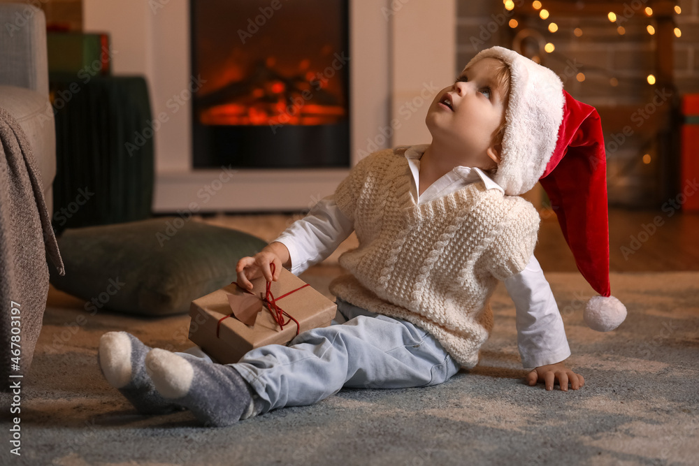 Obraz premium Little boy in Santa hat and with Christmas gift at home