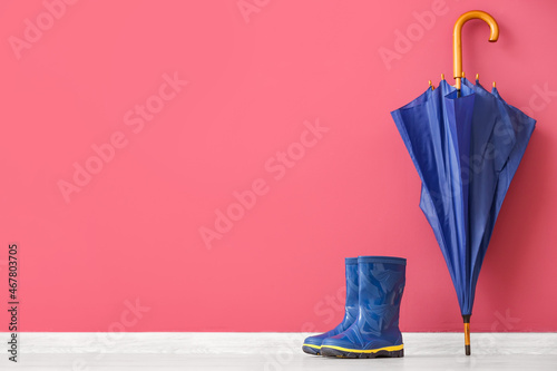 Pair of rubber boots and umbrella on floor against color wall © Pixel-Shot