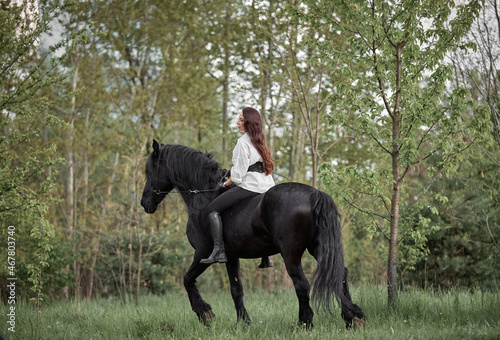 Beautiful long-haired girl riding a Friesian horse