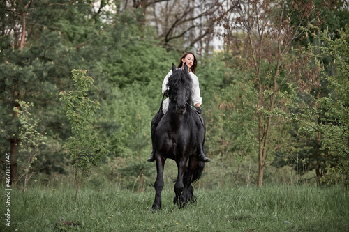 Beautiful long-haired girl riding a Friesian horse