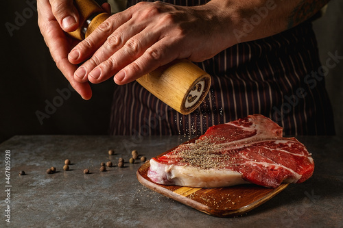 The hands of the chef add fresh pepper from the mill to the beef steak