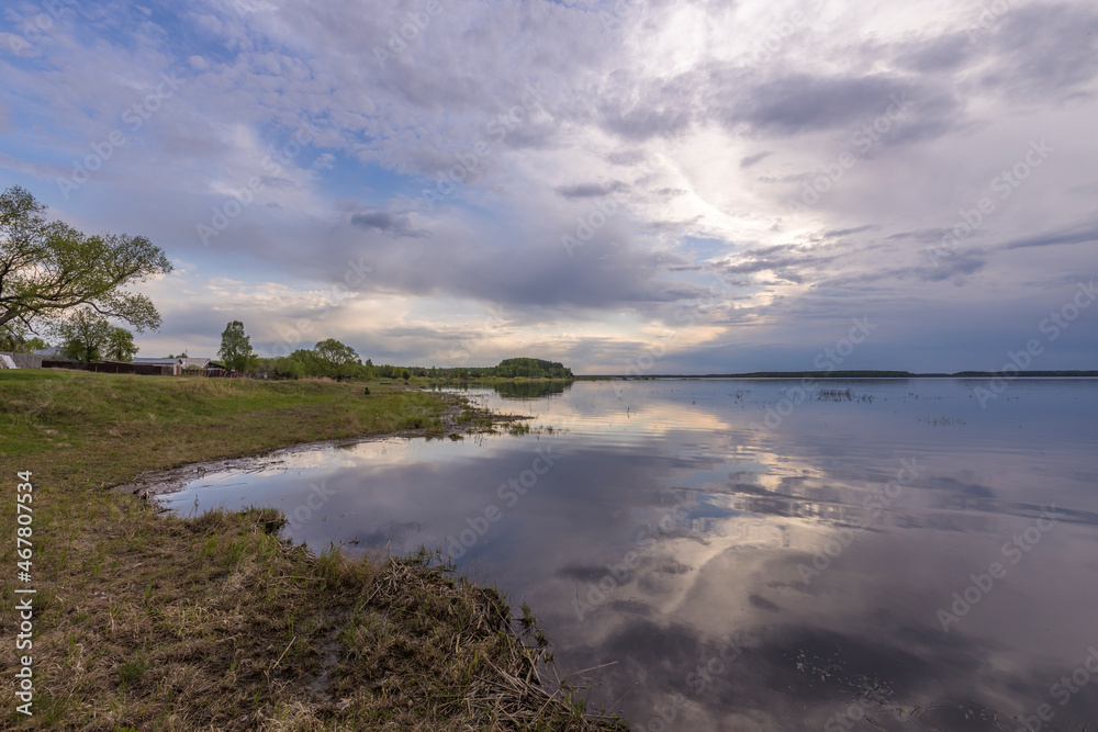 Evening landscape on the lake in early spring. The dramatic sky is reflected in the water. Evening landscape on the lake in early spring. The dramatic sky is reflected in the water.