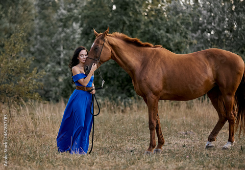 Beautiful long-haired girl in a blue dress with a red horse