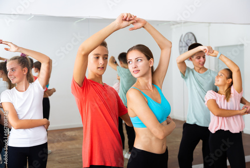 Group of teenage boys and girls training movements of slow foxtrot in dance studio with female coach