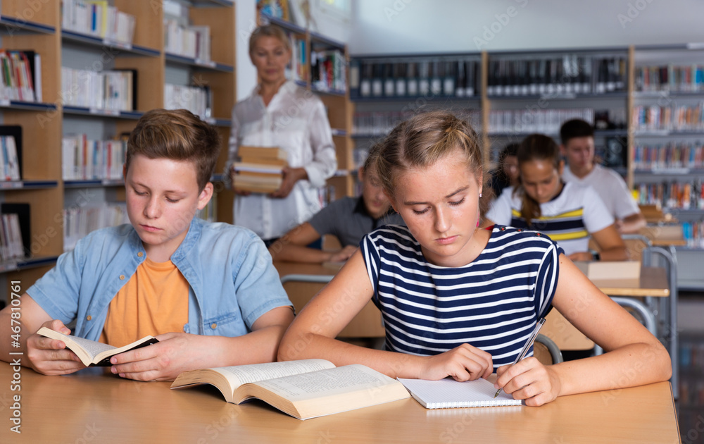 Fototapeta premium Schoolchildren preparing for lesson in school library, reading textbooks