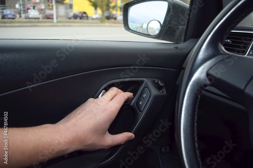 A man's hand opening the door from the car interior on the background of the steering wheel