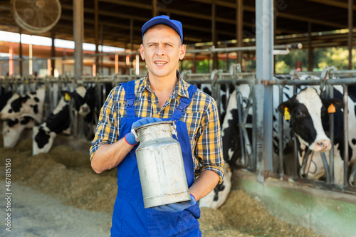 Portrait of smiling farmer standing in cowshed at dairy farm holding aluminium milk churn..