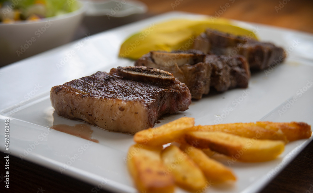 ROASTED BEEF, SERVED ON A WHITE PLATE AND LETTUCE, TOMATO AND CORN SALAD, ACCOMPANIED WITH FRENCH FRIES AND AVOCADO ROASTED BEEF, SERVED ON A WHITE PLATE AND LETTUCE, TOMATO AND CORN SALAD, ACCOMPANIED WITH FRENCH FRIES AND AVOCADO