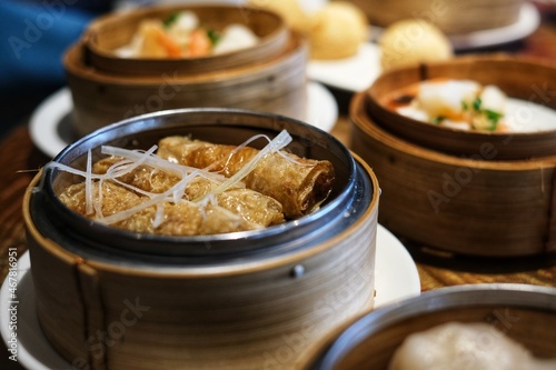 An assorted dishes of fried and steamed dim sum or Chinese dumpling, served in round bamboo steamers on a wooden table at a Chinese restaurant.