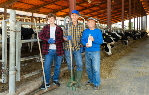 Group photo of senior, adult and young men farmers standing in cowshed.