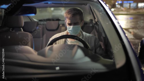 Delivery service man wearing his protective mask due to Covid-19 late nigt with a delivery item in a car. Volunteer Work in the Midst of an Epidemic. Courier with a Cardboard Box Package on a second