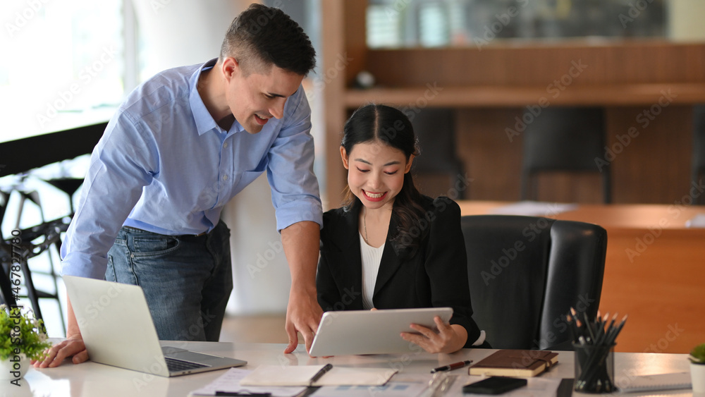 Obraz premium Businesswoman talking and working on tablet with caucasian male boss