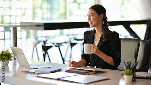 Beautiful asian businesswoman having a tasty morning coffee during work