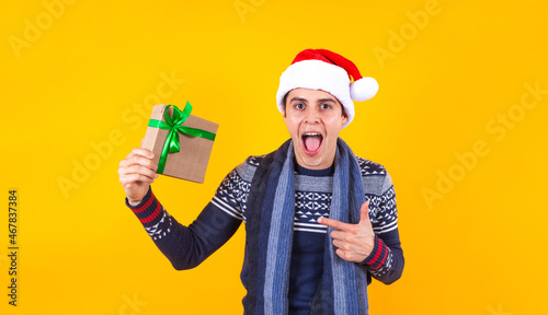 Portrait of young Latin man holding Christmas gift box on a yellow background in Mexico latin america