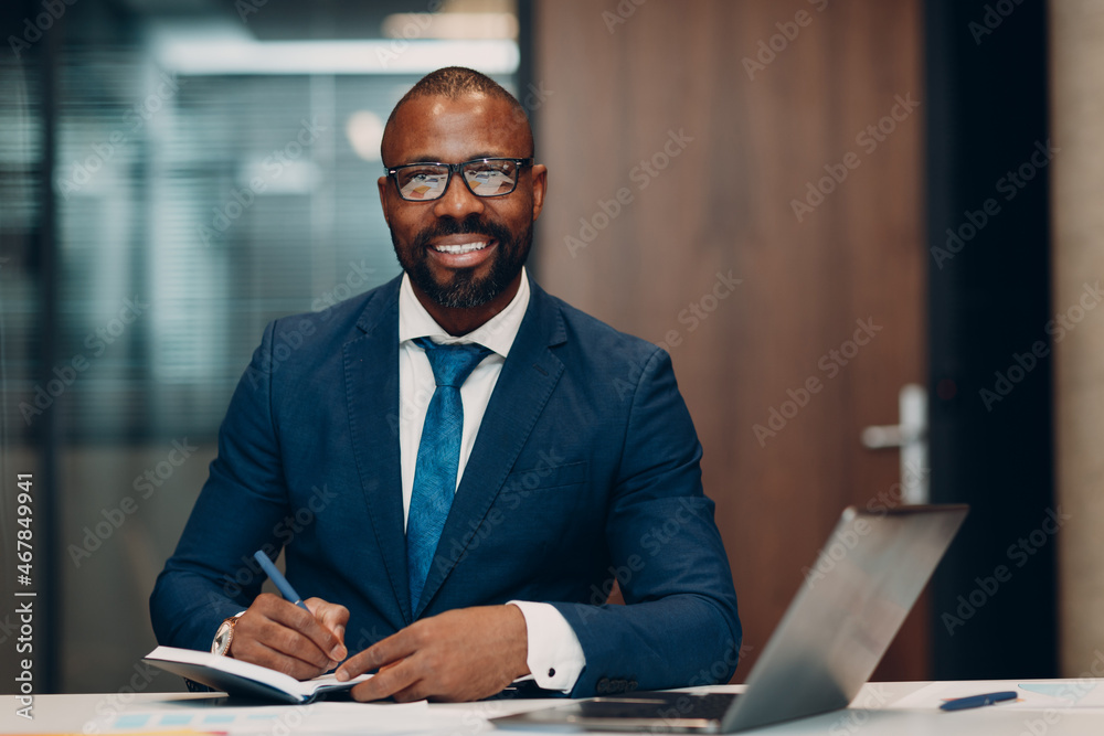 Portrait smiling african american businessman signs contract sit at table for meeting in office with notebook with pen and laptop