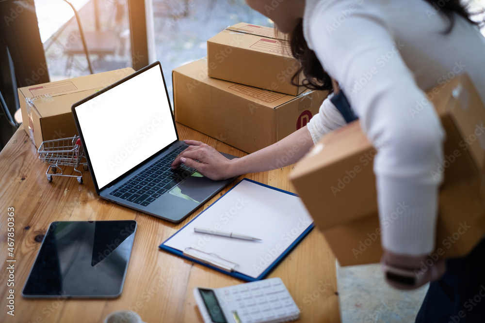 Business owner check customer orders on her laptops and pack products at home. Successful SME entrepreneur concept. Business owner check customer orders on her laptops and pack products at home. Successful SME entrepreneur concept.