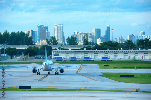 Large white commercial jet airliner airplane on the tarmac at international airport in the evening with Fort Lauderdale skyline in background.