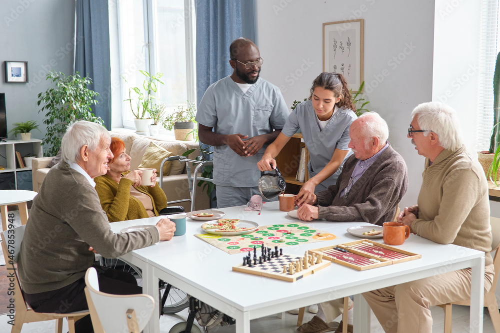 © pressmaster - Nurse and doctor pouring hot tea for senior people while they sitting at the table and playing board games in nursing home © pressmaster - Nurse and doctor pouring hot tea for senior people while they sitting at the table and playing board games in nursing home