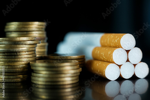 Smoking is a waste of coin money on black background. Cigarettes and TAX concept.