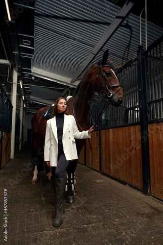 Portrait of smiling female jockey standing by horse in stable