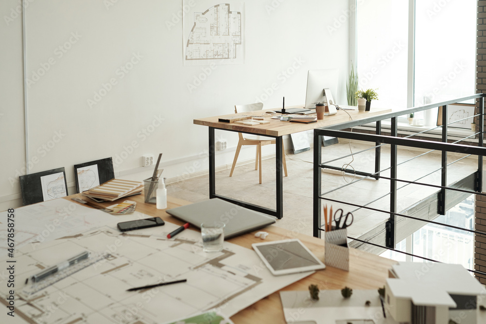 Fototapeta premium Two workplaces consisting on tables with sketches, blueprints, gadgets, samples and other supplies in large contemporary openspace office