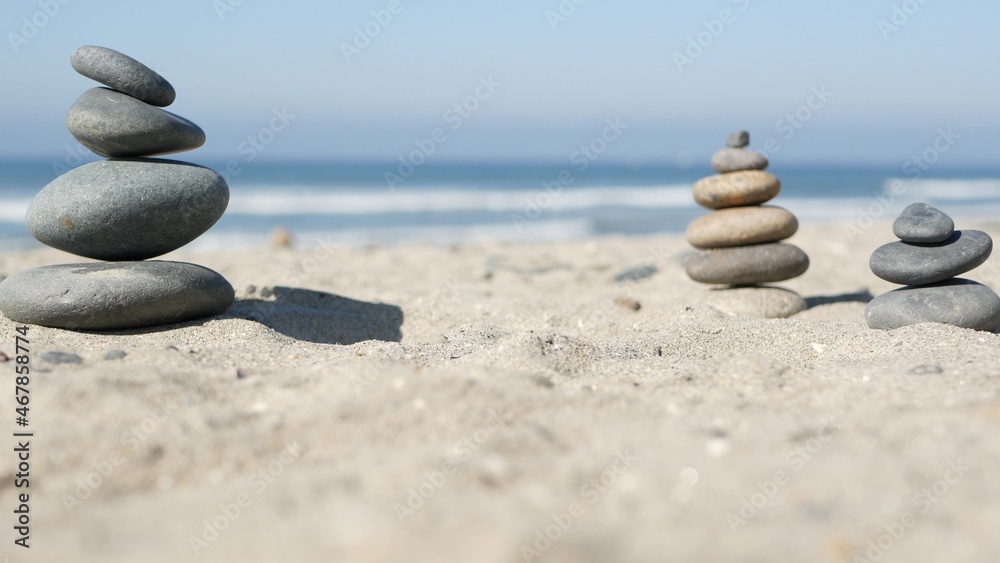 Fototapeta premium Rock balancing on ocean beach, stones stacking by sea water waves. Pyramid of pebbles on sandy shore. Stable pile or heap in soft focus with bokeh, close up. Zen balance, minimalism, harmony and peace