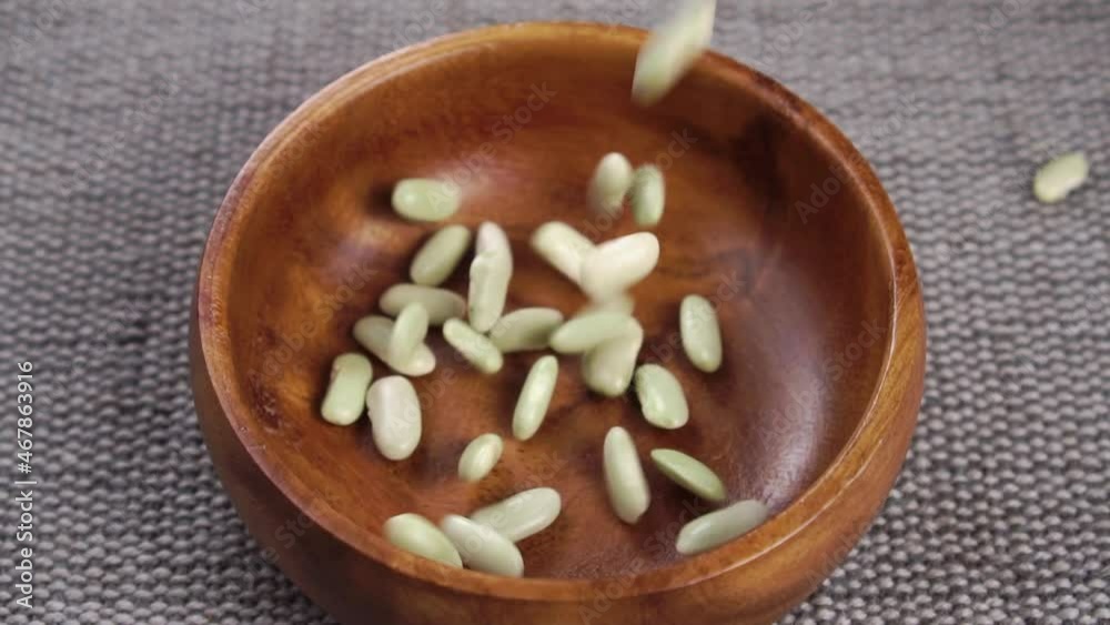 Uncooked green beans fall into a wooden bowl on a gray rustic jute mat close up. Raw legumes. Traditional Spanish mediterranean cuisine Uncooked green beans fall into a wooden bowl on a gray rustic jute mat close up. Raw legumes. Traditional Spanish mediterranean cuisine