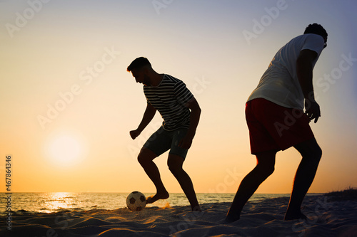 Friends playing football on beach at sunset