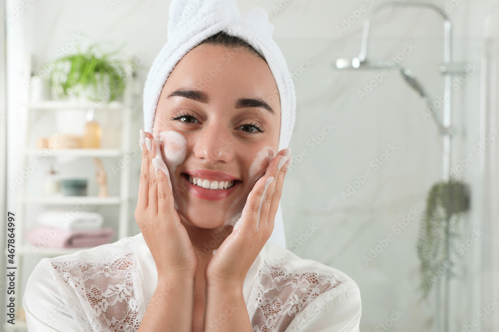 Beautiful young woman applying cleansing foam onto face in bathroom. Skin care cosmetic Beautiful young woman applying cleansing foam onto face in bathroom. Skin care cosmetic
