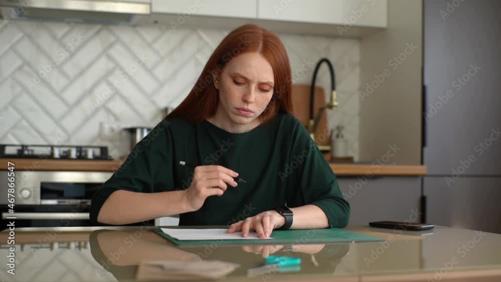 Front view of focused young woman student making mark with pencil on white paper lying on green rubber cutting mat, sitting at desk in kitchen room with light interior. Shooting in slow motion. Front view of focused young woman student making mark with pencil on white paper lying on green rubber cutting mat, sitting at desk in kitchen room with light interior. Shooting in slow motion.