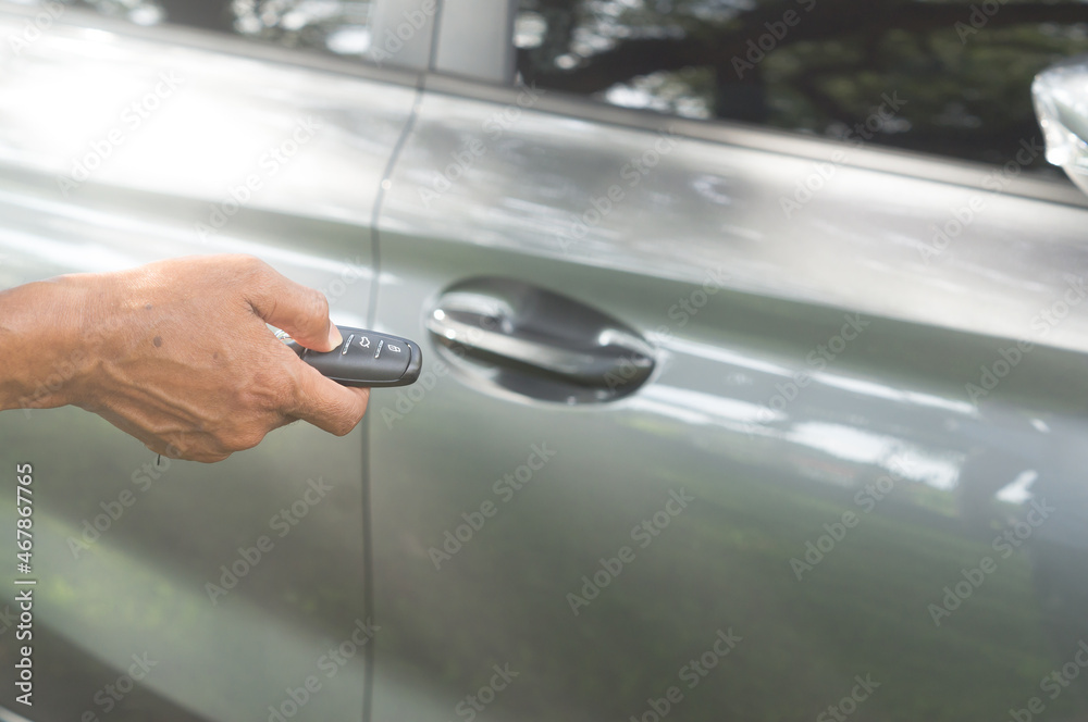 A luxurious car owner using a key remote control to lock, unlock and start car engine, a photo of selective focus with concept of high technological digital key operated car